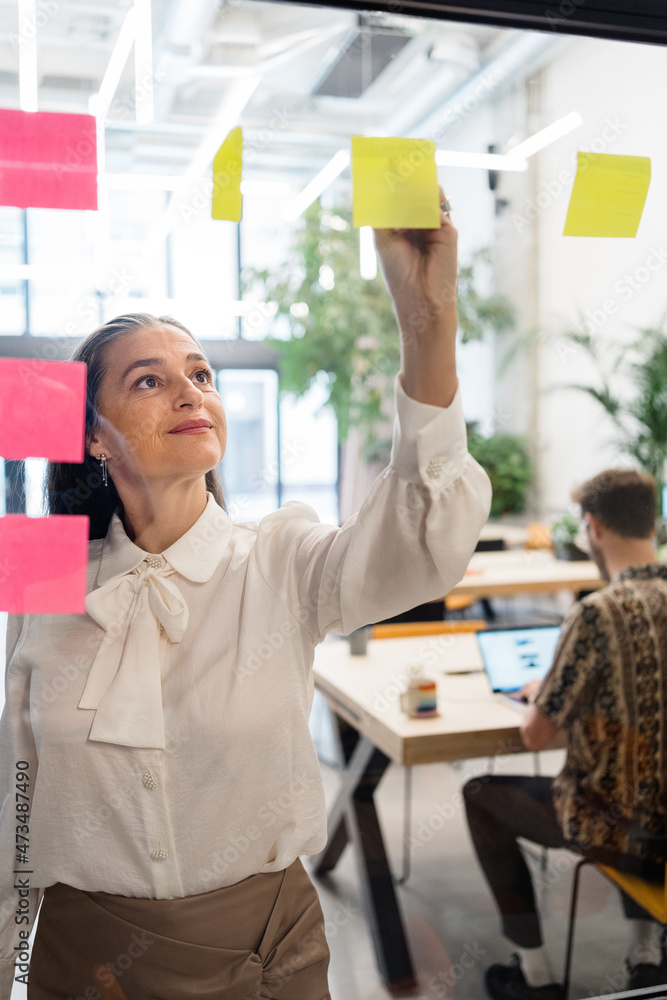 Woman writing on stickers near diverse coworkers