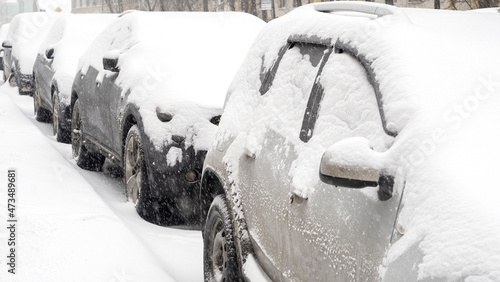 Row of cars covered by snow during heavy snowfall, snow storm in the city