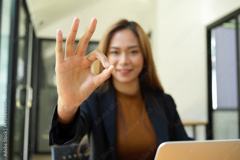 Business worker posting OK hand sign at her desk.