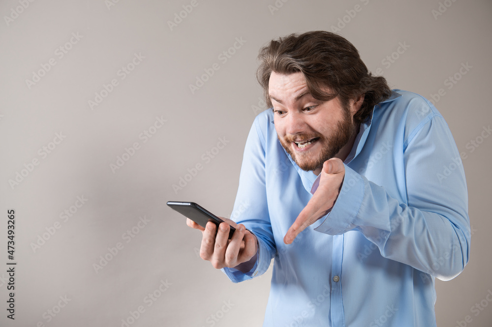 Aggressive young business man in blue shirt shouting into his mobile phone on grey background Aggressive young business man in blue shirt shouting into his mobile phone on grey background