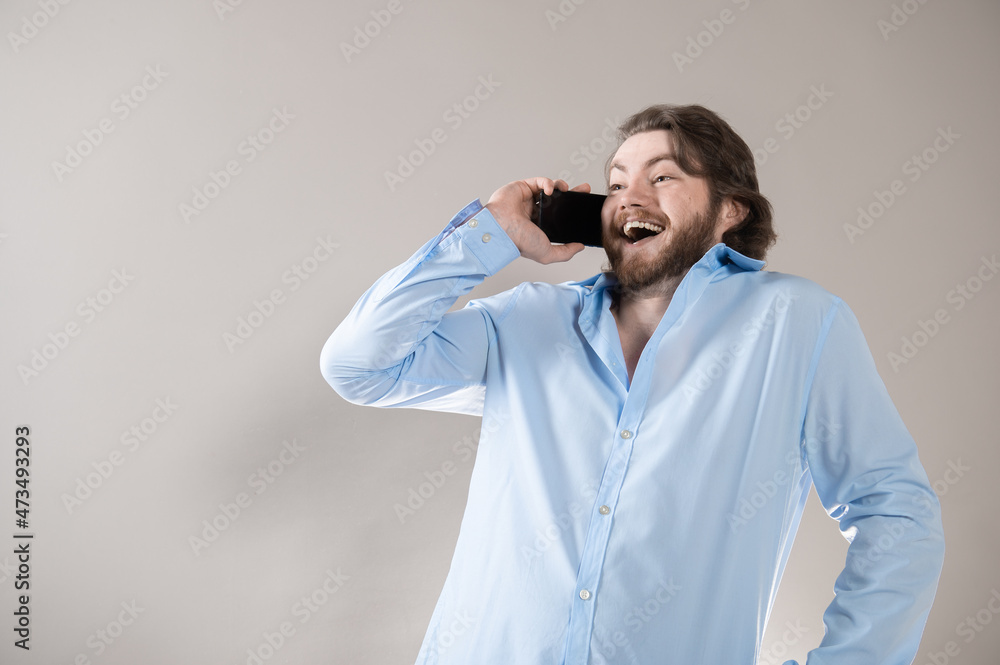 Young bearded man having call and talking on smartphone with pleasure isolated over grey background Young bearded man having call and talking on smartphone with pleasure isolated over grey background