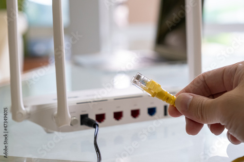 Selective focus at Lan cable socket of the router with people hand plug the fiber cable into internet router.  High speed internet for personal use with computer and technology. photo