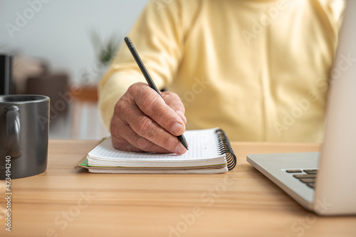 Man writing on the notebook of his day planner while working at the laptop from home