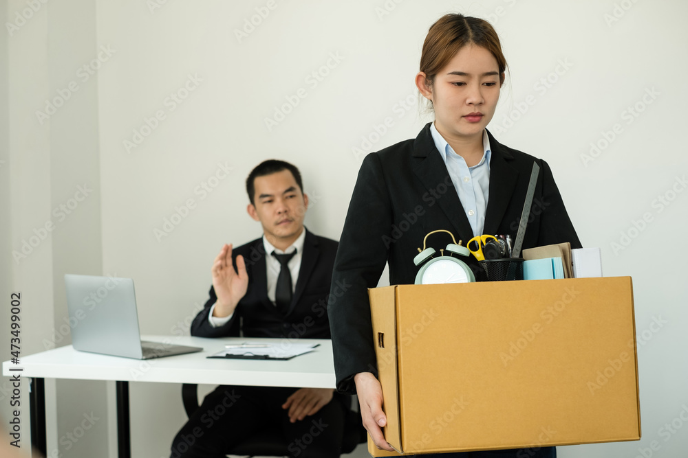 A woman office worker is unhappy with being fired from a company packing things into cardboard boxes. The Young woman was stressed and disappointed by being fired. concept of layoffs and unemployment