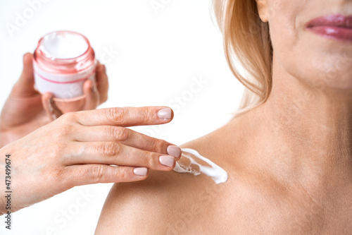 Cosmetologist applying body cream on shoulder of the mature woman