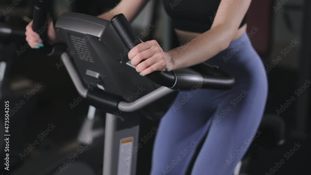 A young athletic woman is engaged in an exercise bike. She's wearing leggings. Cardio training in the gym. 4K A young athletic woman is engaged in an exercise bike. She's wearing leggings. Cardio training in the gym. 4K