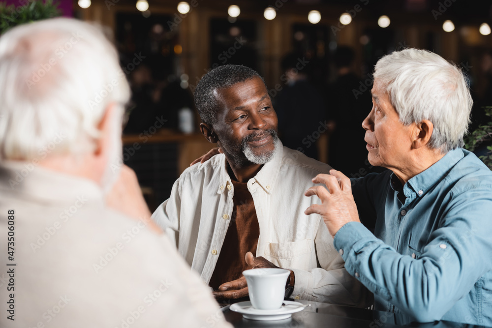 senior asian man talking and gesturing during meeting with multiethnic friends in cafe senior asian man talking and gesturing during meeting with multiethnic friends in cafe
