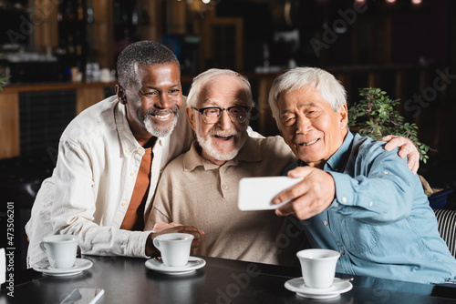 senior asian man taking selfie with happy multiethnic friends in restaurant