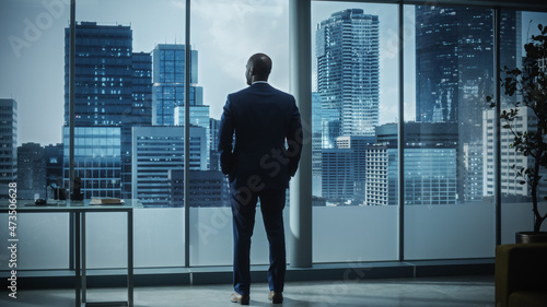 Bild auf Leinwand Thoughtful African-American Businessman in a Perfect Tailored Suit Standing in His Office Looking out of the Window on Big City