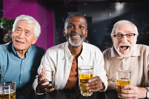 thriller senior multicultural men watching football match near glasses of beer in pub