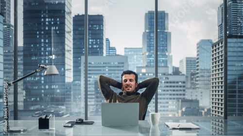 Portrait of Relaxed Brilliant Businessman Working on Laptop Computer in His Big City Office. Charismatic Laid-back Entrepreneur Leaned Against the Back of the Chair and Chill.