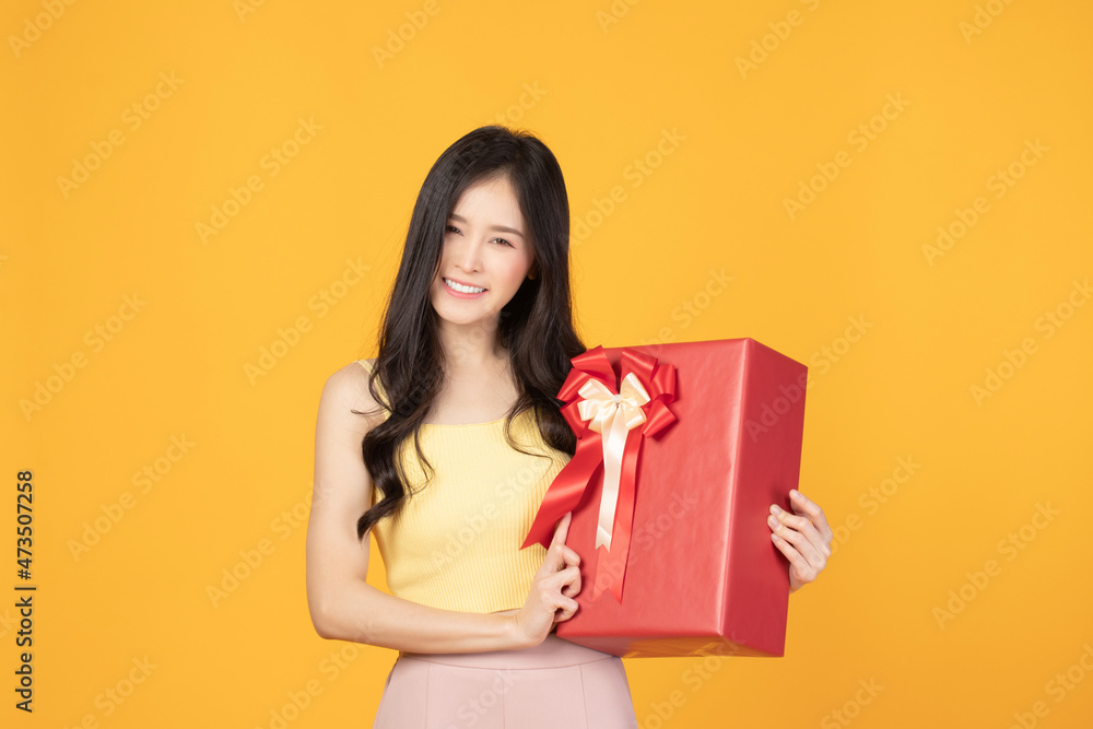 Portrait of happy smiling girl in casual holding gift box and expression face isolated over yellow background Portrait of happy smiling girl in casual holding gift box and expression face isolated over yellow background