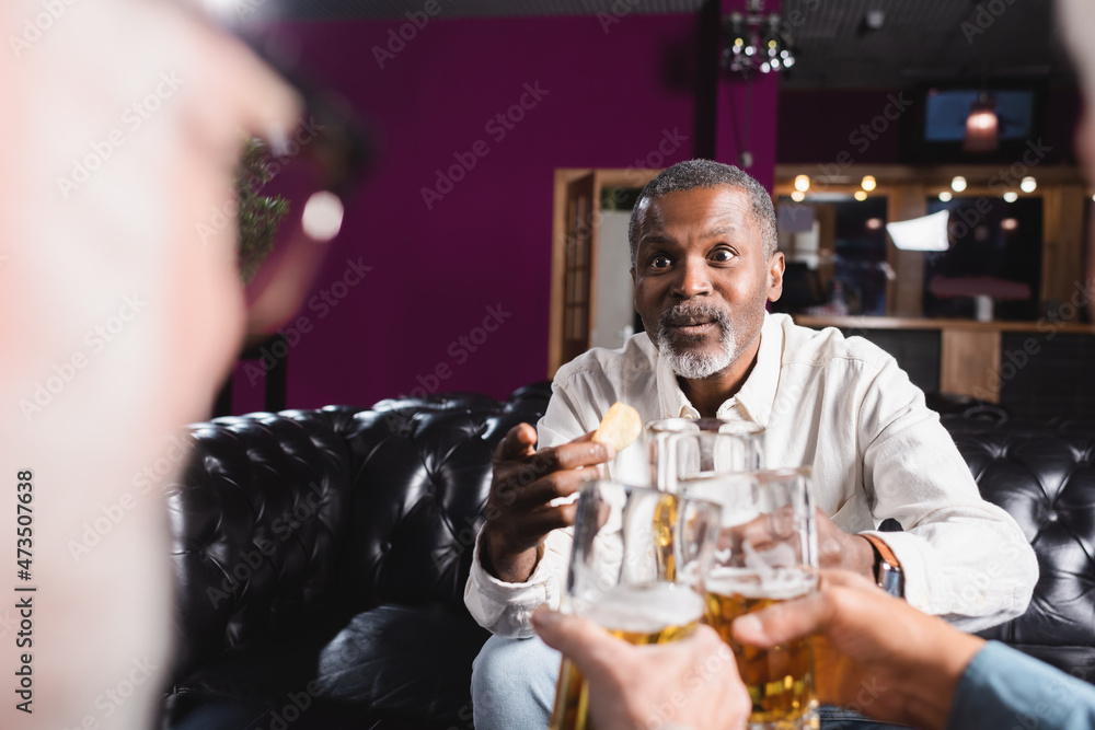 custom made wallpaper toronto digitalsurprised african american man pointing with finger while clinking beer glasses with blurred friends