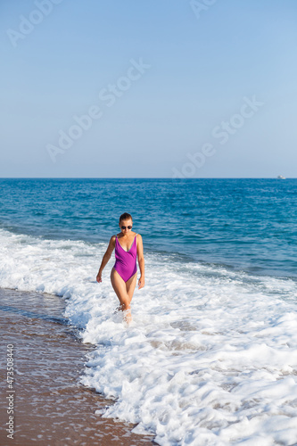 A young beautiful woman with a toned body in a bright swimsuit walks along the sandy beach. Summer vacation at the sea. Mediterranean Turkish Sea. Selective focus