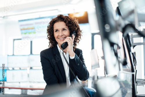 Smiling businesswoman talking on landline telephone in control room photo