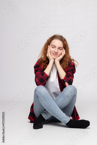 a young pretty girl is sitting on a white background in a plaid shirt