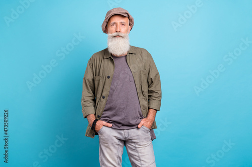 Photo of style white beard elder man stand wear khaki cap shirt isolated on blue color background