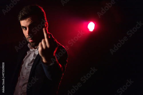 Close up photo of man showing middle finger on pink and black background.