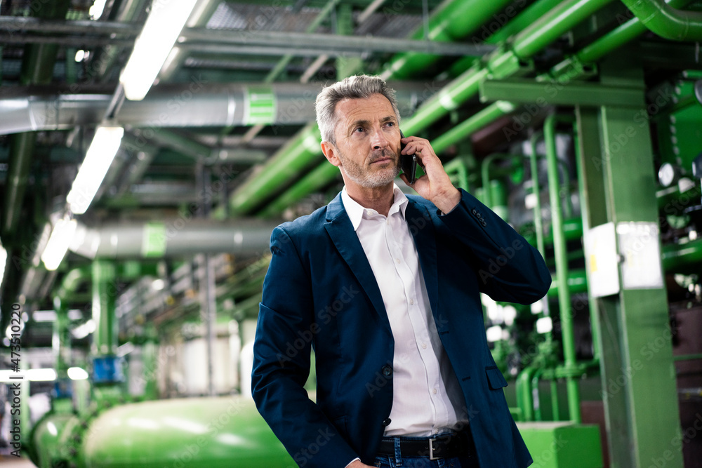 Businessman talking on smart phone while standing in industry Businessman talking on smart phone while standing in industry
