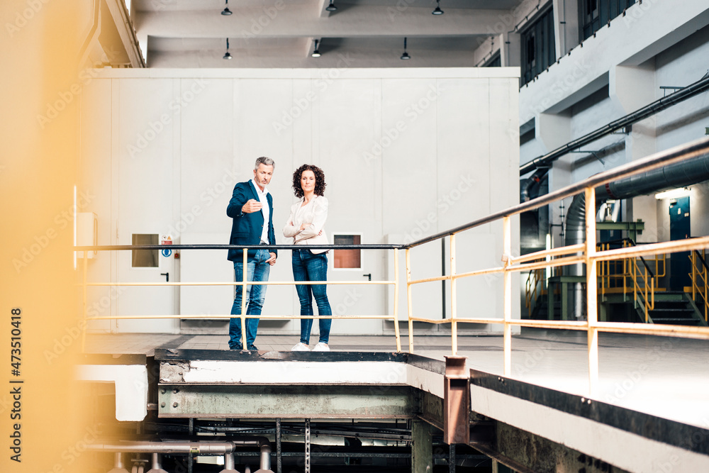 Businessman explaining colleague while standing by railing in industry Businessman explaining colleague while standing by railing in industry