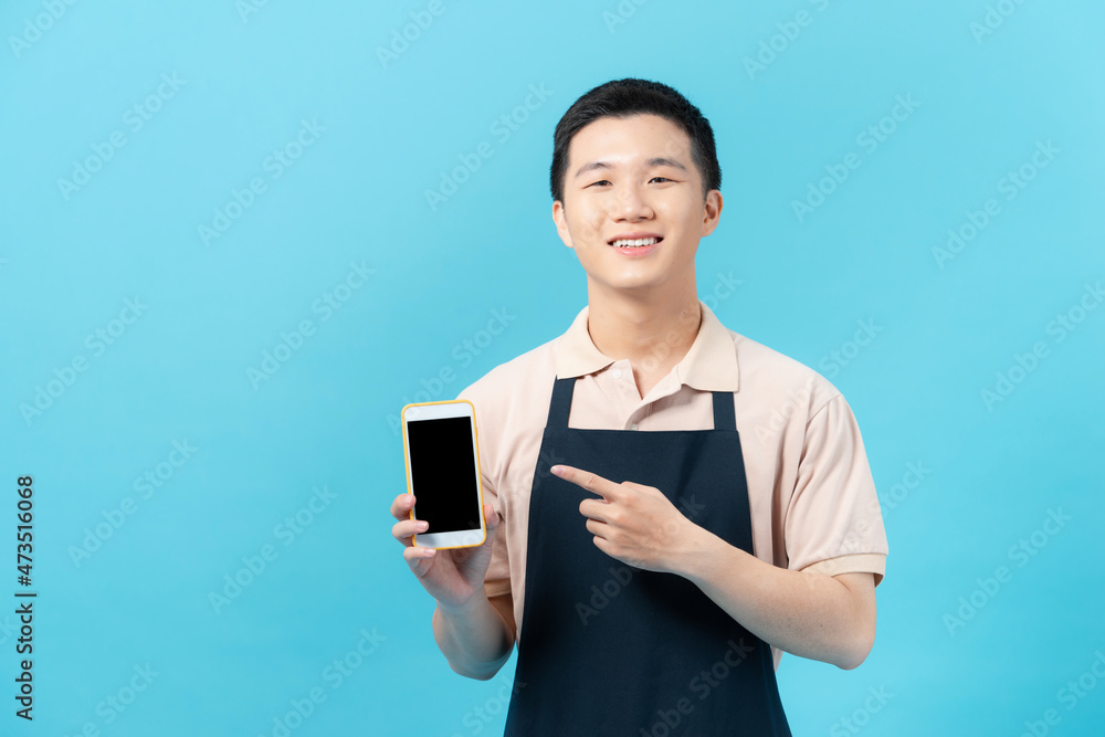 shopman standing with apron uses a smart phone isolated on blue background shopman standing with apron uses a smart phone isolated on blue background