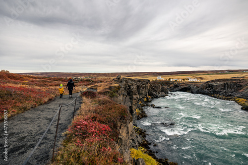 Mother and son in yellow jacket walking next to a river at Goðafoss Waterfall Iceland