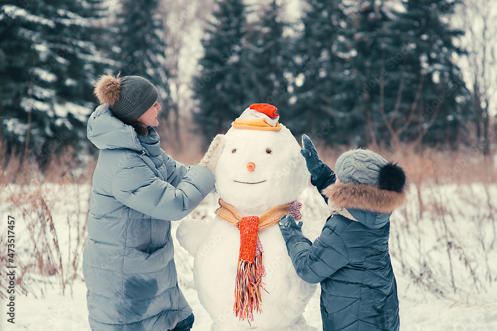 Mom and daughter make a snowman in the winter snowy forest Mom and daughter make a snowman in the winter snowy forest