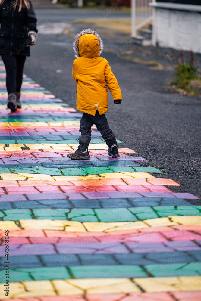 Preschool kid walks the Seyðisfjörður - Seydisfjördur Rainbow Street in a yellow jacket on a rainy day Preschool kid walks the Seyðisfjörður - Seydisfjördur Rainbow Street in a yellow jacket on a rainy day