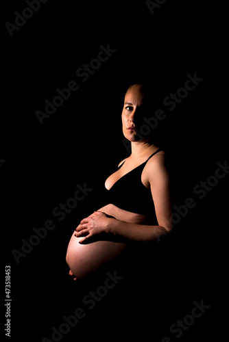 Portrait einer schwangeren Frau in schwarzem Top vor schwarzem Hintergrund photo