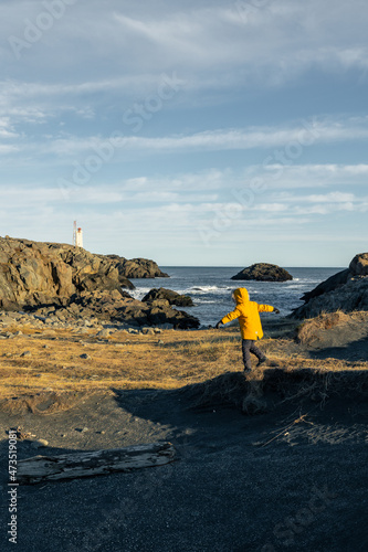 Liitle boy in yellow jacket balancing at Arnastapi Cliff Iceland with blue sky and single clouds photo