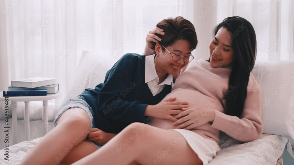 Pregnant Asian lesbian woman and her partner are happy to spend time together at home. Pregnant Asian lesbian woman and her partner are happy to spend time together at home.