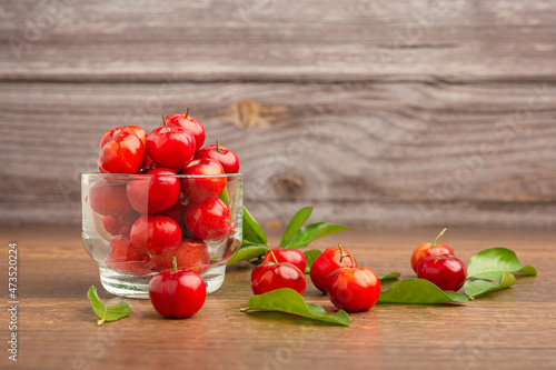 Photos Ripe red acerola cherries in glass and green leaves scattered on a wooden table