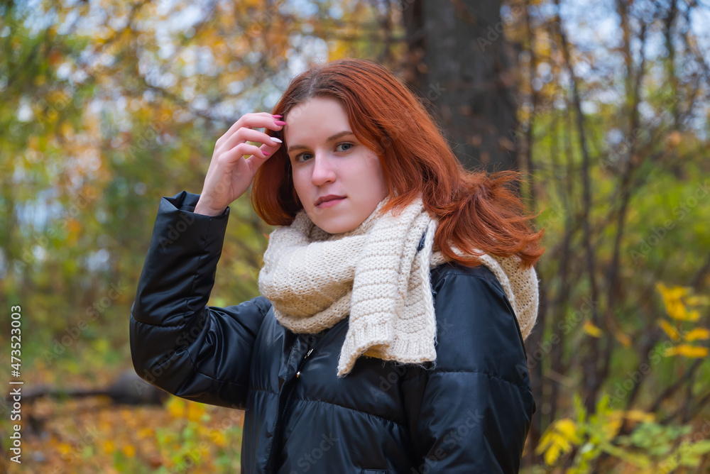 portrait of a red-haired smiling girl in a jacket straightens her hair with her hands. against the background of autumn nature, the concept of human emotions portrait of a red-haired smiling girl in a jacket straightens her hair with her hands. against the background of autumn nature, the concept of human emotions