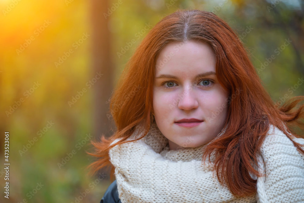 portrait of a red-haired smiling girl in a jacket and scarf against the background of autumn nature and bright sun concept of human emotion