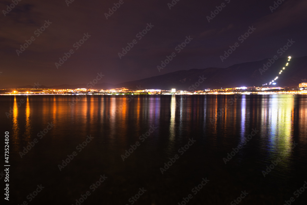 Night city with lights and mountains by the sea and red sky.