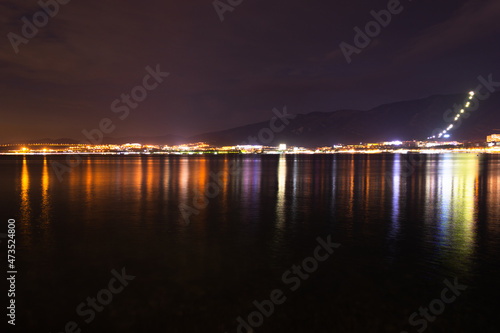 Night city with lights and mountains by the sea and red sky. © Aleksandr