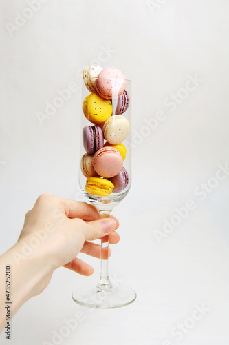 Mini colorful french macarons in a champagne glass in hand, white background. Holiday aesthetic