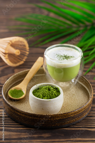 Matcha tea powder with whisk and palm branch on a wooden table.