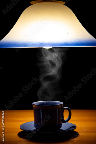 A teacup on the table under a lighting chandelier, on a black background