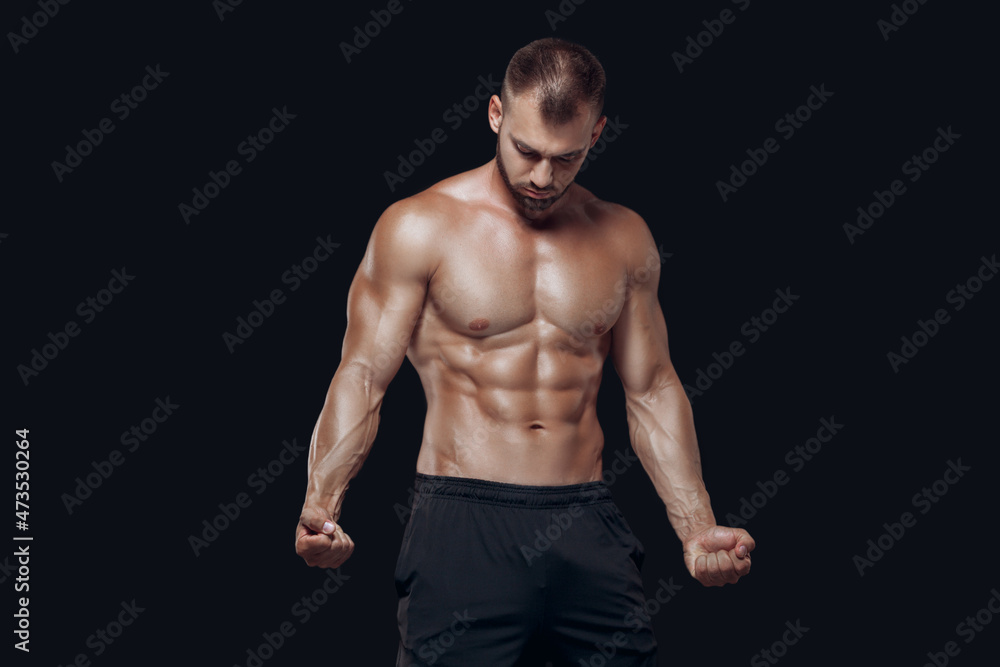 Young muscular and fit young bodybuilder fitness male model posing and demonstrating his muscles isolated on black background