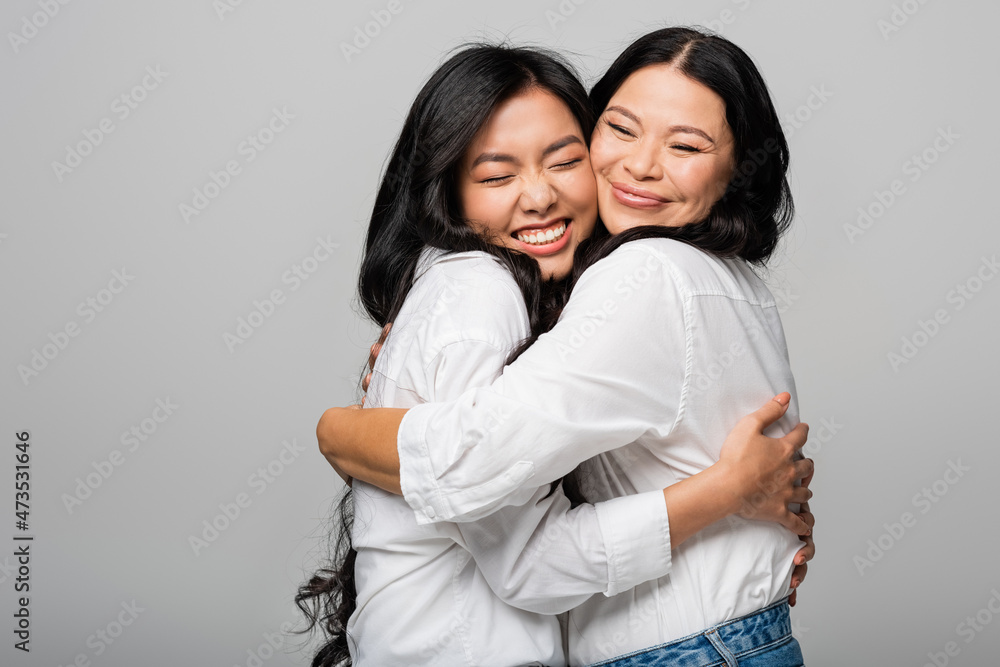 pleased asian mother and daughter in white shirts hugging isolated on grey pleased asian mother and daughter in white shirts hugging isolated on grey
