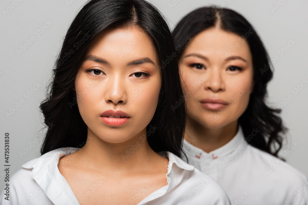 asian young adult daughter near blurred mother standing behind isolated on grey asian young adult daughter near blurred mother standing behind isolated on grey