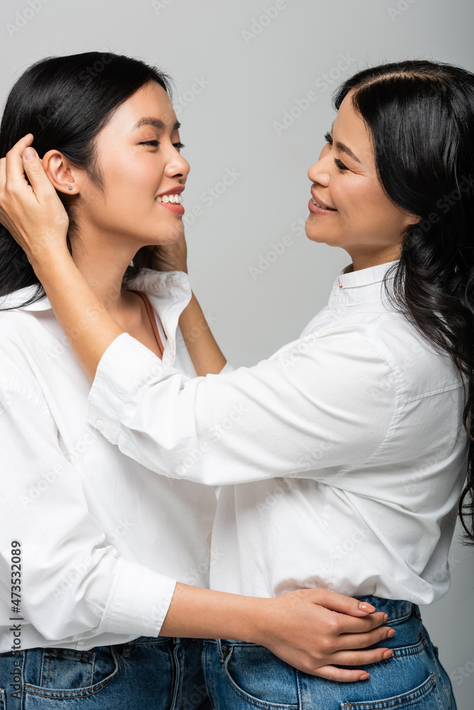 happy asian mother adjusting hair of positive young adult daughter isolated on grey happy asian mother adjusting hair of positive young adult daughter isolated on grey