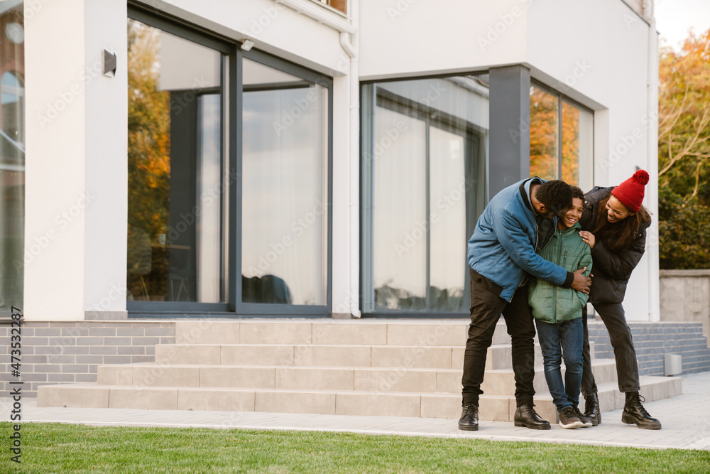 Black family smiling and hugging together while standing by house