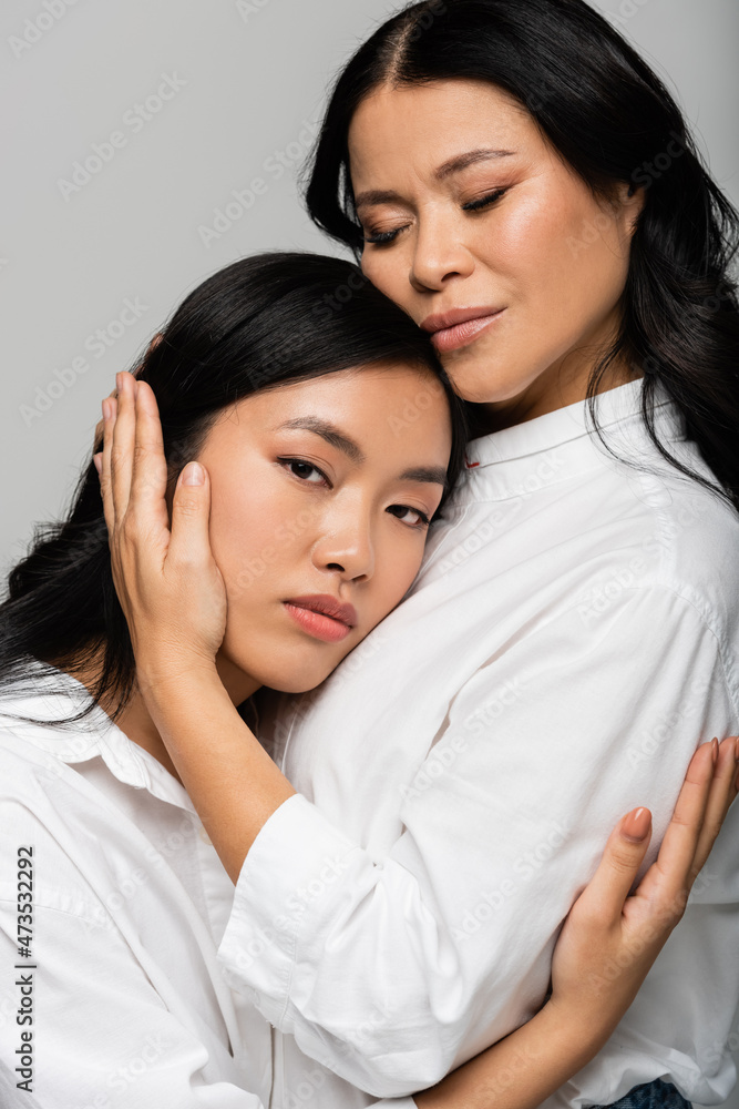 caring asian mother hugging young daughter isolated on grey caring asian mother hugging young daughter isolated on grey