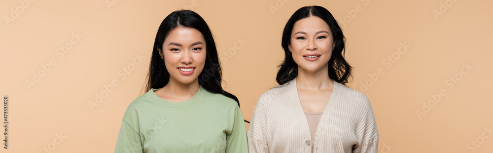 cheerful asian mother and adult daughter looking at camera isolated on beige, banner cheerful asian mother and adult daughter looking at camera isolated on beige, banner
