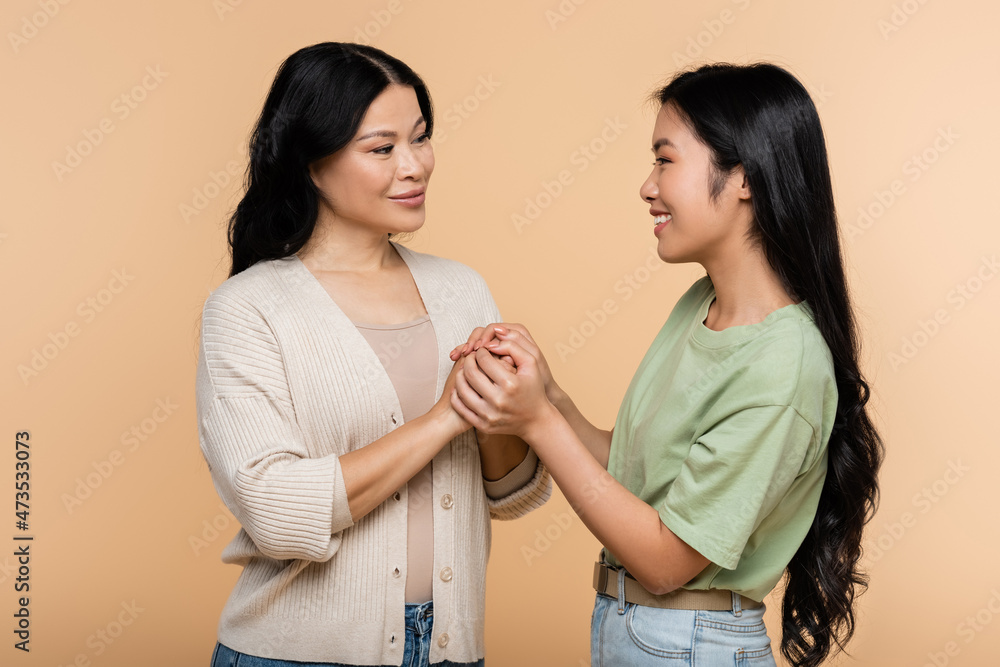 happy asian woman holding hands with adult daughter isolated on beige happy asian woman holding hands with adult daughter isolated on beige