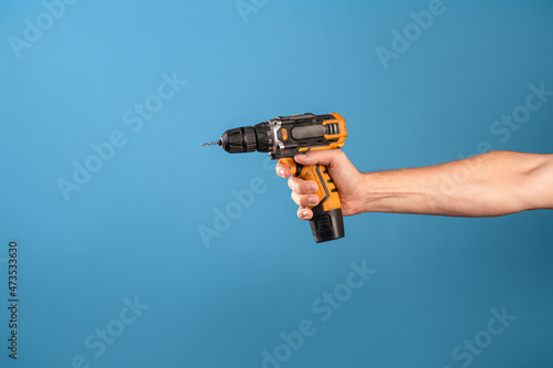 Fix it, fix a malfunction or tighten a bolt on a construction site. A man's hand holds a screwdriver or drill, a repair tool, a photo on a blue background.