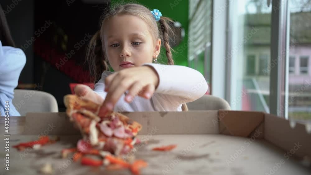 Hungry child girl 5-6 years old eating pizza in a restaurant reaches out and takes out the last piece of pizza from the box. The family is having fun together. Hungry child girl 5-6 years old eating pizza in a restaurant reaches out and takes out the last piece of pizza from the box. The family is having fun together.