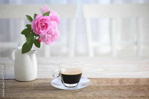 Coffee in glass cup and pink rose on wooden table indoor